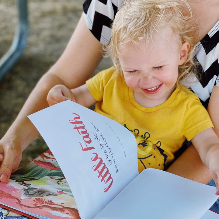 Little boy sitting in mother's lap reading children's book Little Faith