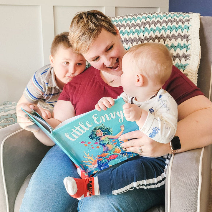 Mother reading to her baby boy and son the children's book Little Envy